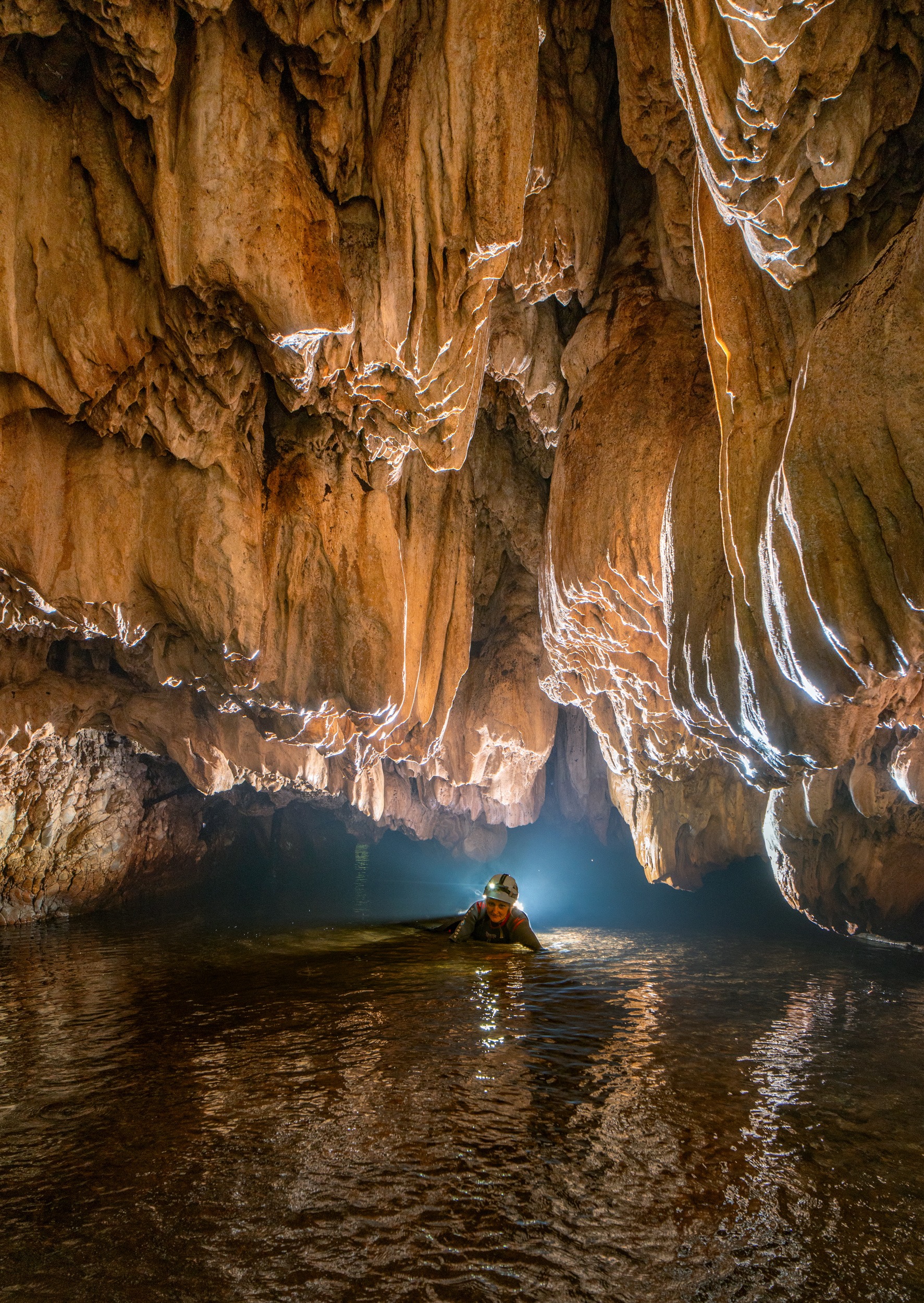 Caver in underground water beneath a sculpted rock ceiling near Siderocastro